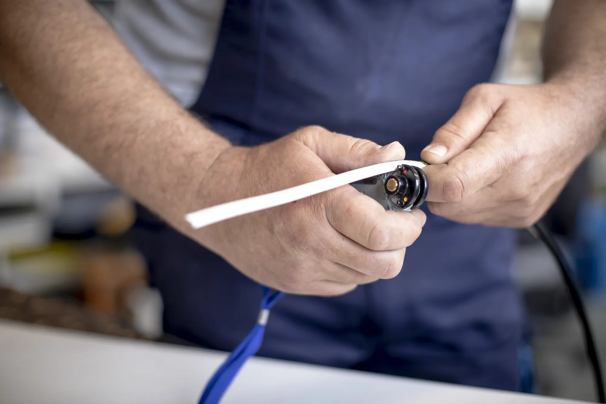 Ein Mann in blauer Arbeitslatzhose hantieren an einem Band mit einem weißem Band